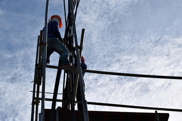 Filipino Construction steel workers assembling steel bars on high-rise building with no proper protective suits and safety shoes. underside view, silhouettes