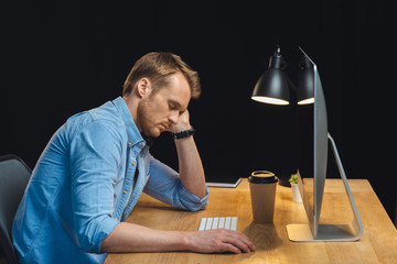 Obraz premium side view of businessman sleeping at table with computer and paper coffee cup during night time in office