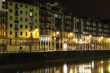 Fototapeta na wymiar The Shore Alley (Paseo de la Ribera) in Bilbao, Basque Country, Spain, during a winter night, with typical basque houses with yellow lights reflecting