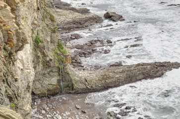 A landscape of rocks on the high cliffs on a rough sea during a cloudy rainy day from Paseo de la Galea in Getxo town, in the Basque Country, Spain
