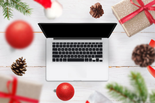 Christmas gifts and decorations come out of the laptop. An empty screen of the device for the mockup, web site design promotion. Top view of a wooden wooden desk.