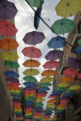 The sun shelter of an open air street through a series of coloured opened umbrellas hanged on cables, with a blue cloudy sky, in Orihuela, Spain