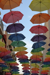 The sun shelter of an open air street through a series of coloured opened umbrellas hanged on cables, with a blue cloudy sky, in Orihuela, Spain