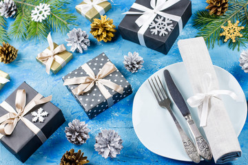 Christmas table setting with plates, silverware, gift box and decorations on blue table