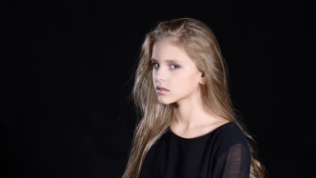 Children and feelings. Beautiful blond long-haired girl looking at camera emotionally. Model teenaged girl on dlack background posing. 4k