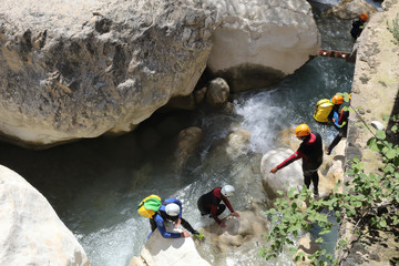 People practicing canyoning in the Vero river canyon, with helmets, protections and diving suits among the rocks during summer in Alquezar, Spain