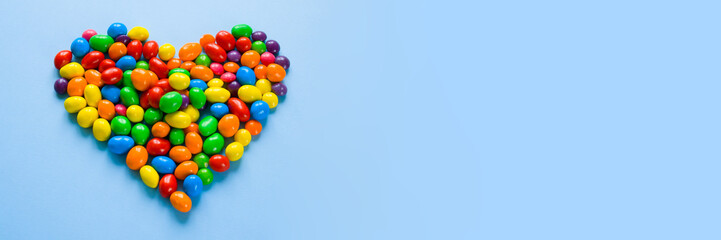 Colorful candies arranged as heart on blue background