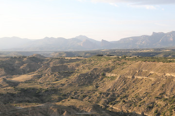 A landscape of the Aragon fields and mountains during a late summer afternoon, with blue sky, yellow tilled soil and pine trees in Montearagon, Spain