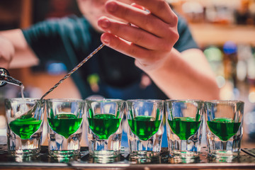 Green liquid in shot glasses standing on the counter. bartender preparing shots