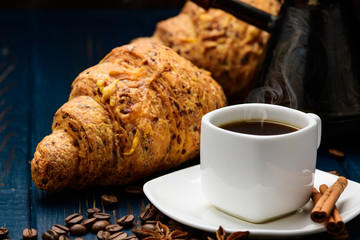 coffee pours into a Cup on a blue wooden table with coffee beans and a croissant