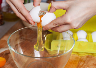 Female hands cracking raw egg into glass bowl