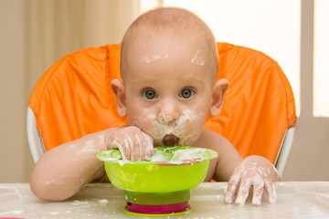 A baby boy in a orange high chair eating yoghurt