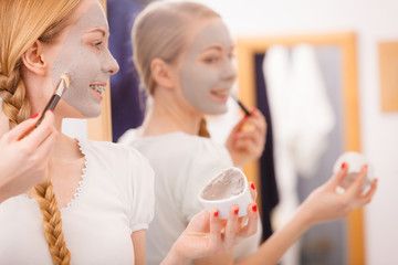 Happy young woman applying mud mask on face