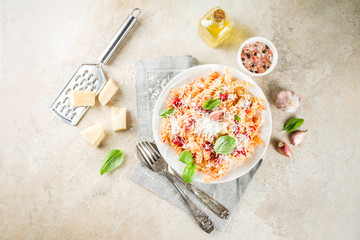 Italian food, fusilli pasta with  tomato sauce, grated parmesan cheese and basil, light stone table copy space top view