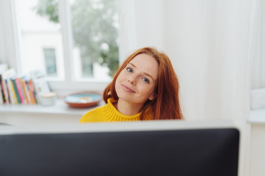 Smiling ginger girl sitting in front of monitor
