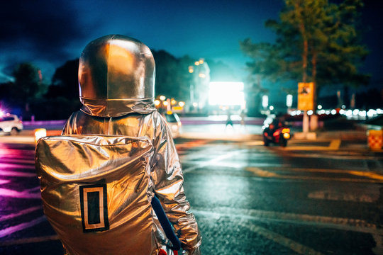 Rear view of spaceman on a street in the city at night attracted by shining projection screen