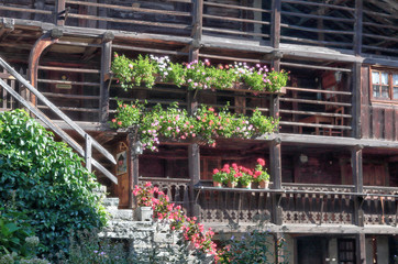 Fototapeta na wymiar A typical Walser lodge, made of stone and with board wooden balconies with flower planters and staircase, in Val d'Otro valley, Alps mountains, Italy