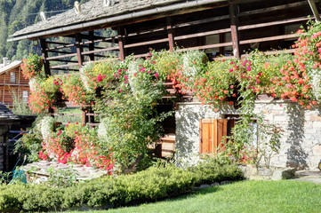 A typical Walser lodge, made of stone and  with board protected wooden balconies with flower planters, in Val d'Otro valley, Alps mountains, Italy