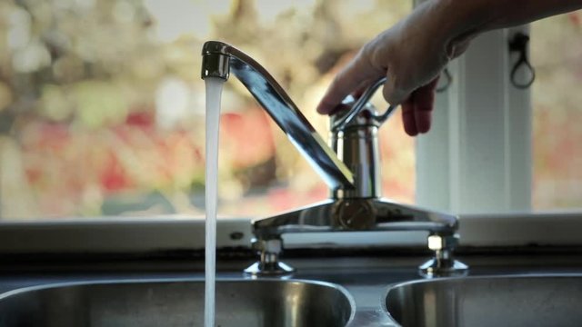 Person having a glass of water. Checking temperature with finger before filling a glass with water.