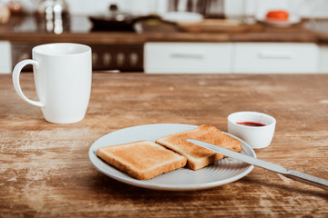 selective focus of toasts on plate, jam and coffee cup at table in kitchen