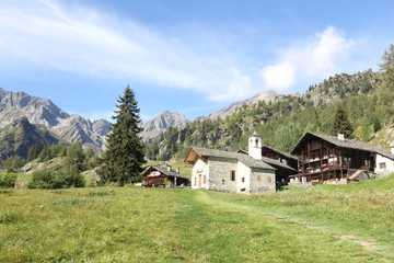 Fototapeta na wymiar The Walser town of Follu, with wood and stone lodges, high mountains, forests and pastures, in summer, in Val d'Otro valley, Alps mountains, Italy