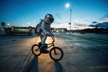 Spaceman in the city at night on parking lot riding BMX bike