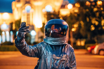 Spaceman on a street in the city at night holding smartphone