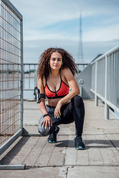 Portrait of young athletic woman with earbuds crouching outdoors