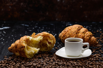 coffee pours into a Cup on a blue wooden table with coffee beans and a croissant