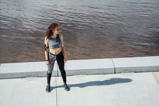 Young athletic woman wearing earbuds standing at the riverside
