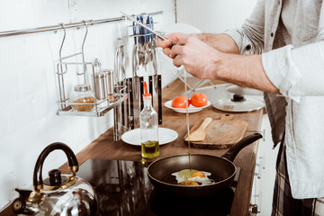 partial view of young man cooking scrambled eggs on breakfast in kitchen