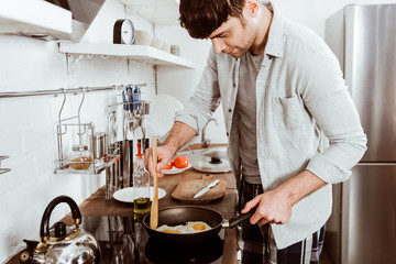 handsome young man making eggs on breakfast in kitchen at home