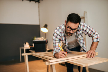 Young handsome man marking and measuring wood.