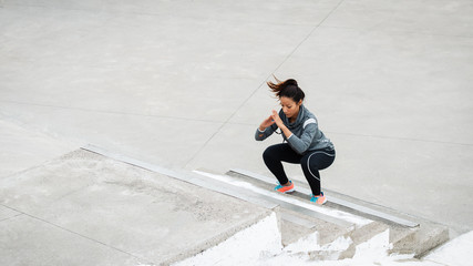 Latin urban sporty woman training. Female athlete doing squat jumps on urban stairs.