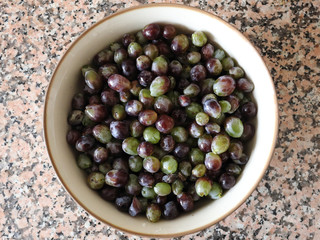 A white ceramic bowl containing red and green wet grapes without the stalks, on a marble surface