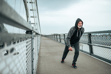 Fit male senior running across the bridge with his hood on.