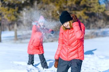 Outdoor portrait of two young girls in bright jackets, playing snowballs in a winter park. having fun throwing snow