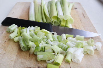 A bunch of clean, fresh and wet leek vegetables, already detached and ready to be cut, minced and sliced, on a light wooden board with a knife