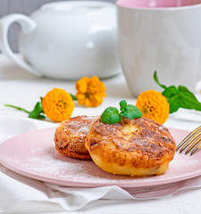 Cottage cheese pancakes on a pink plate, sprinkled with powdered sugar