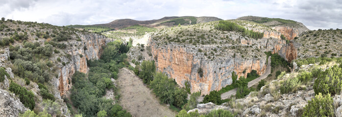 The Barranco de la Hoz Seca (Dry Defile Gully) canyon, with scarps, bushes and red rocks, in a cloudy atumn, in the Jaraba rural town, Aragon, Spain