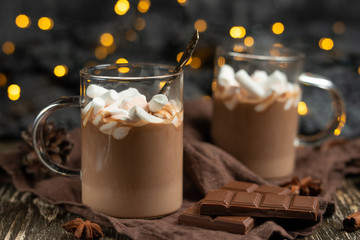 Rich winter hot chocolate with cinnamon sticks and walnuts, chocolate bars in a transparent mug on...