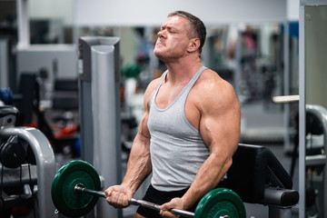 athletic man trains in the gym. Training biceps with a barbell
