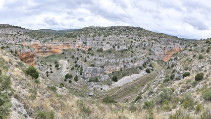 Fototapeta na wymiar The Barranco de la Hoz Seca (Dry Defile Gully) canyon, with scarps, bushes and red rocks, in a cloudy atumn, in the Jaraba rural town, Aragon, Spain
