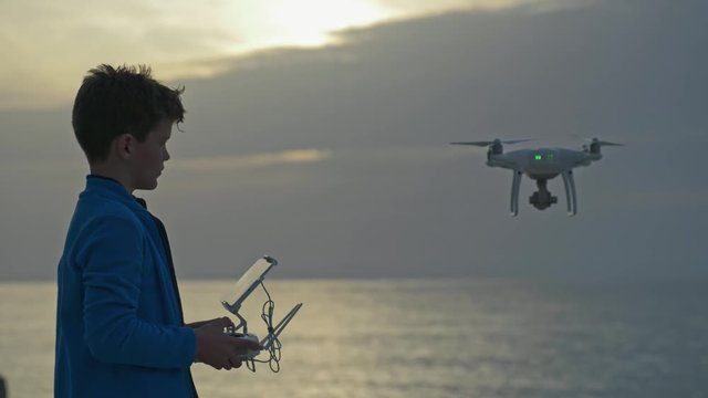 Boy operating drone with remote control. Quadro copter drone flying over sunset sea