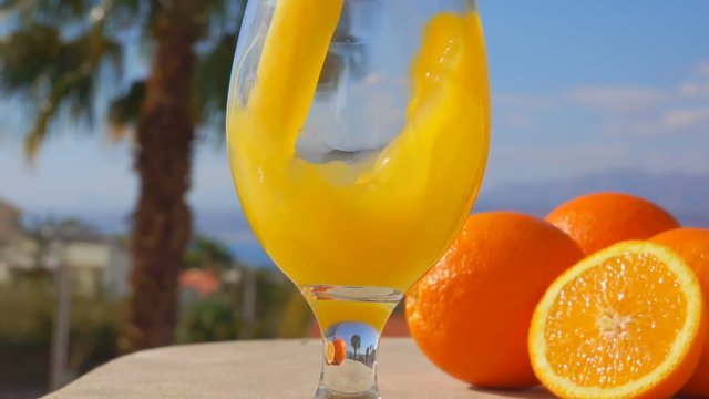 Orange juice is poured into a wine-glass against the background of the sunny sea landscape, close-up camera motion