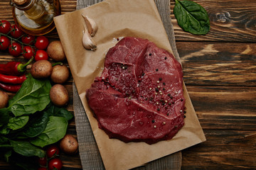 flat lay with fresh raw meat on baking paper with vegetables and spinach on wooden background