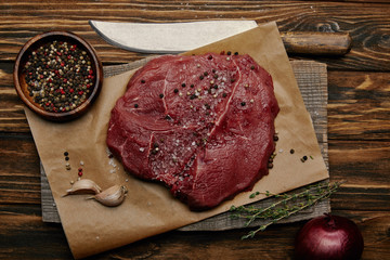 flat lay with fresh raw meat on baking paper with spices and knife on wooden background