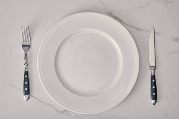 empty plate with fork and knife on white marble background