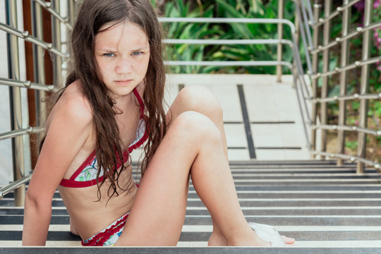 Sad girl in swimsuit with pursed legs sitting on large staircase.