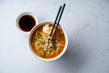 Overhead image of easy japanese ramen with noodles, pork broth, egg and leek in white bowl on concrete background with copy space